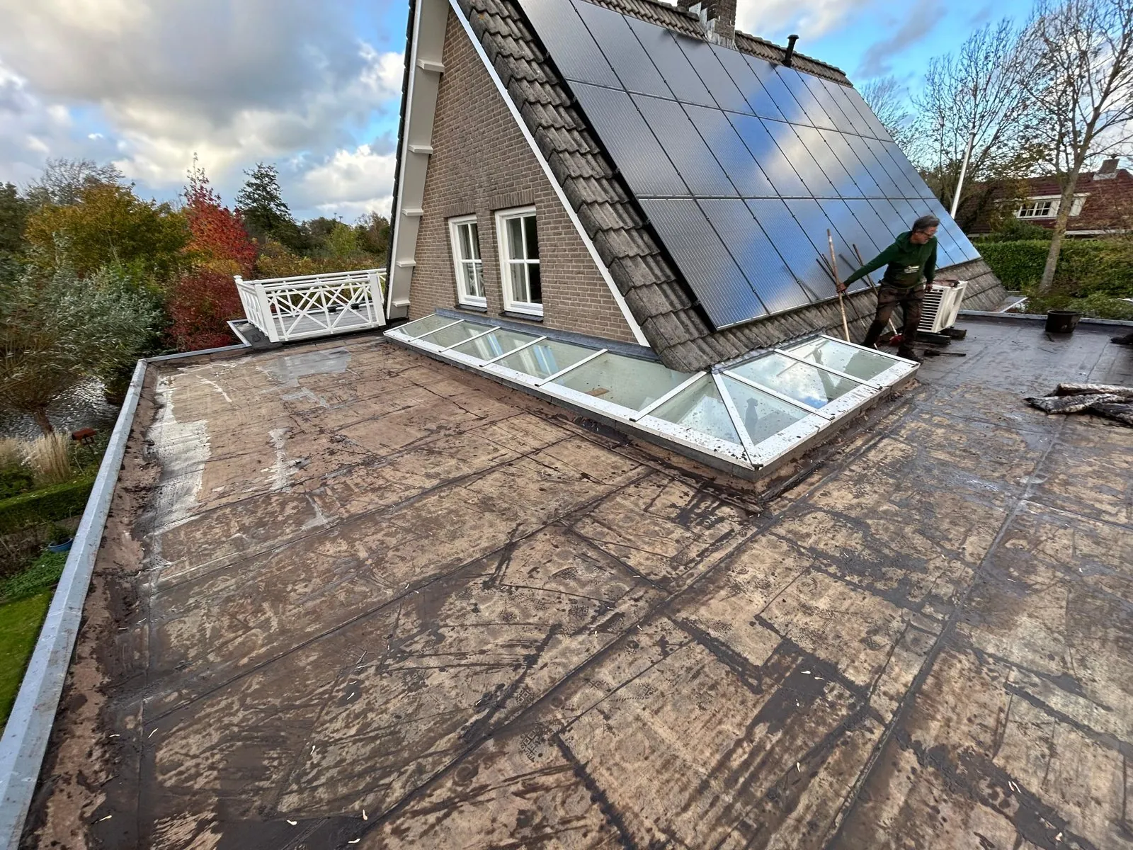 Plat dak met kale bitumen dakbedekking naast een woning met zonnepanelen, vóór de aanleg van een groen dak